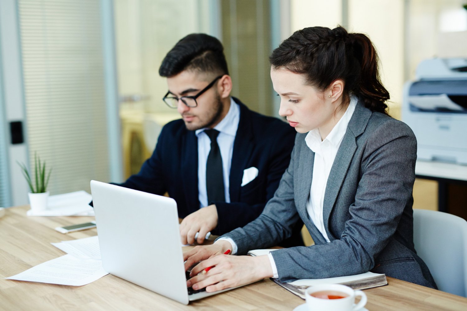 Two colleagues working on financial documents and a laptop in an office
