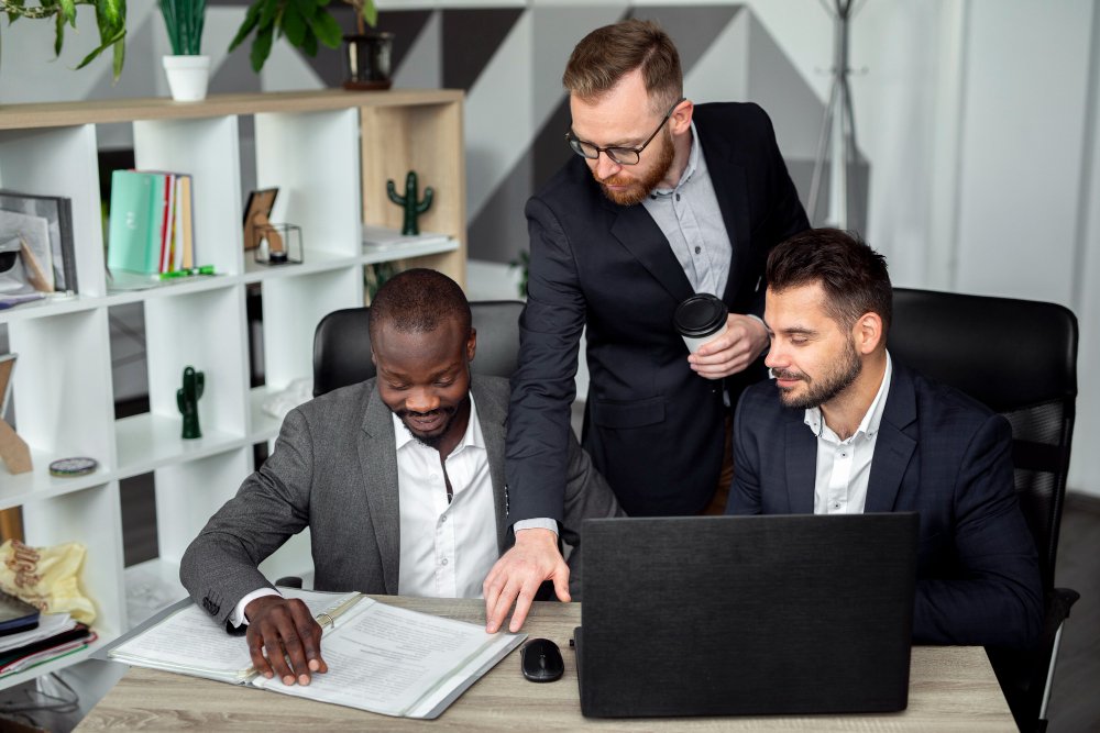 Three colleagues reviewing financial records together on a computer, one holding coffee